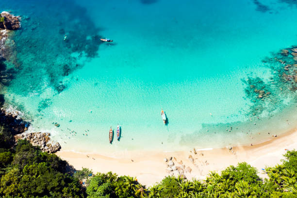 View from above, stunning aerial view of a beautiful tropical beach with white sand and turquoise clear water, long-tail boats and people sunbathing, Banana beach, Phuket, Thailand.