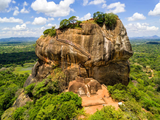 Aerial view from above of Sigiriya or the Lion Rock, an ancient fortress and a palace with gardens, pools, and terraces atop of granite rock in Dambulla, Sri Lanka. Surrounding jungles and landscape.