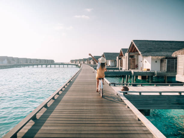Tropical vacations, young woman with bicycle on wooden pier in the Maldives. Female enjoying bike ride on jetty over coral reef water. Dreamlike destination