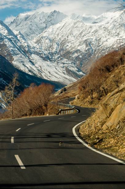 Scenic winter view from the asphalt road in the mountains covered with snow and trees on the side of the road on a background of blue sky and clouds