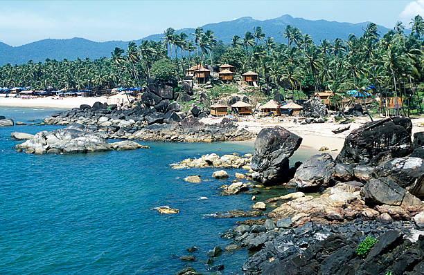 Tropical bay, Palolem beach, white sand, bamboo huts, palm trees, rocks, mountains, Goa, India.