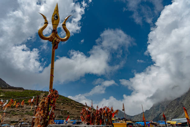 July25th2024, Himachal Pradesh, India. Religious red cloths (chunri) and tridents (trishul), symbols of Lord Shiva, against Kailash Parvat during the Mani Mahesh Kailash Yatra, a Hindu and Buddhist pilgrimage.