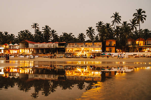 A vibrant beachfront view showcasing restaurants and serene reflections surrounded by lush palm trees during twilight in Goa, India.
