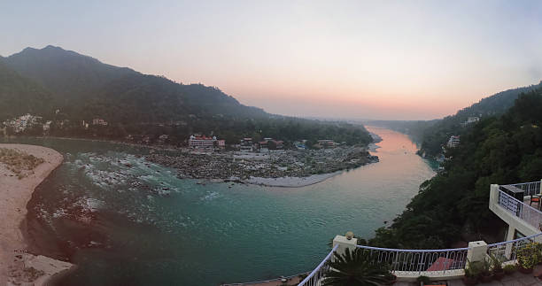 A serene sunset scene over the sacred Ganga River in Rishikesh, India. The golden light reflects on the water as the sun dips behind the Himalayan foothills, creating a peaceful and spiritual atmosphere. Ideal for themes of nature, travel, spirituality, and Indian culture.